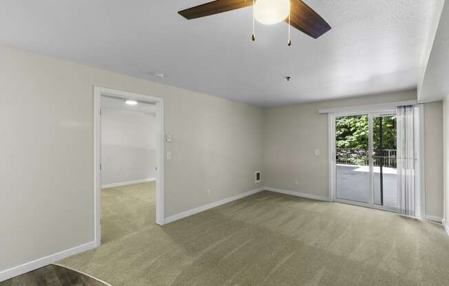 an unfurnished living room with a ceiling fan, cozy carpeting, and sliding glass doors leading to the balcony at West Mall Place Apartment Homes, Everett, WA