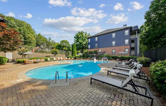 A swimming pool surrounded by a brick patio and lounge chairs.