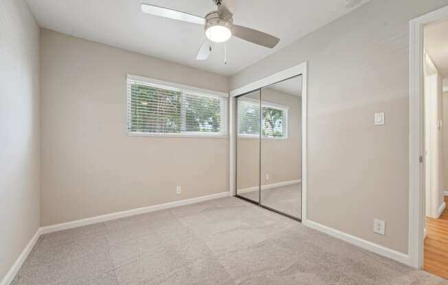 an empty living room with a ceiling fan and a mirrored closet