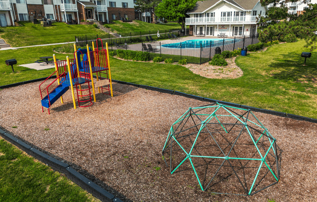 a playground in the backyard of a home with a pool in the background