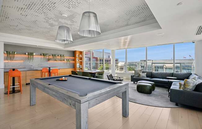 A billiard table is in the middle of a room with a black couch and a green ottoman.