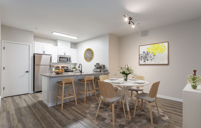 a dining area with a round table and chairs and a kitchen in the background