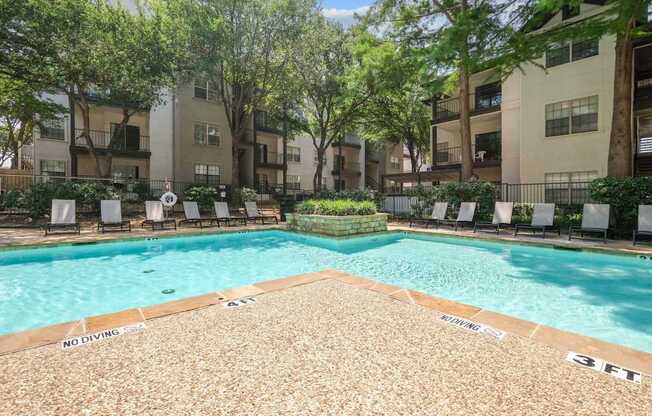 Sparkling pool surrounded by apartment buildings and pool loungers at Jefferson Place apartments in Irving, TX