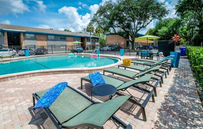 Green lounge chairs next to Community pool at the Watermarc Apartments in Lakeland, Fl with metal side tables and tropical blue towels.