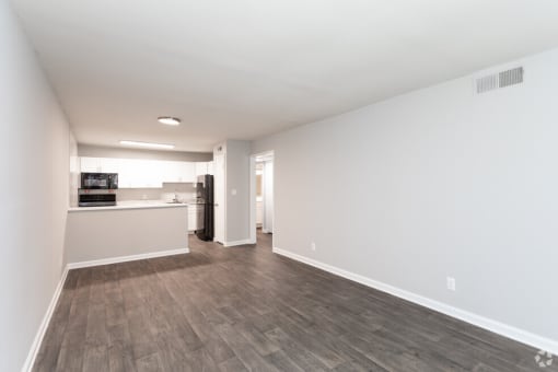 the living room and kitchen of an apartment with white walls and wood floors