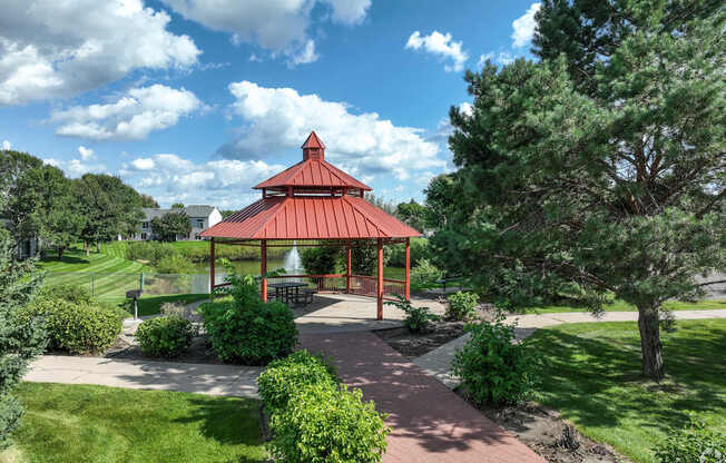 A gazebo is surrounded by greenery and a brick walkway.