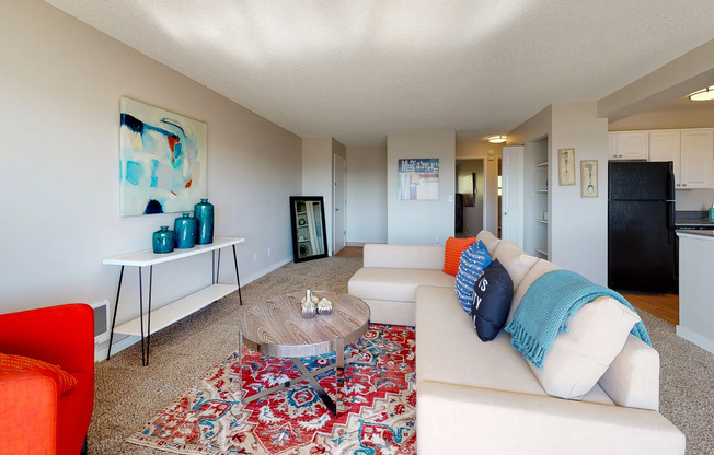Renton WA Apartments for Rent - Sunset View - Carpet, Nude Sectional Couch, Wooden Circle Coffee Table, Blue, and Red Area Rug, and Mult-Colored Decorative Pillows