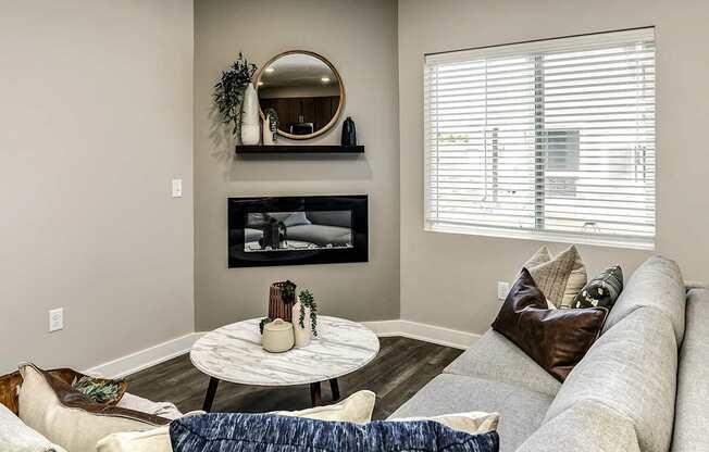 A living room with a grey couch, a round table, and a fireplace.