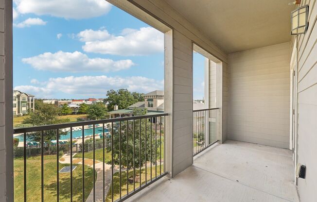 A balcony with a black railing and a pool in the distance.