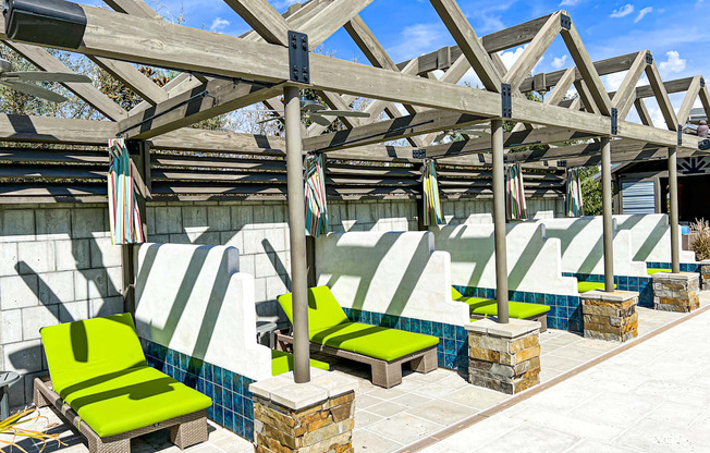 a group of green lounge chairs under a roof next to a pool