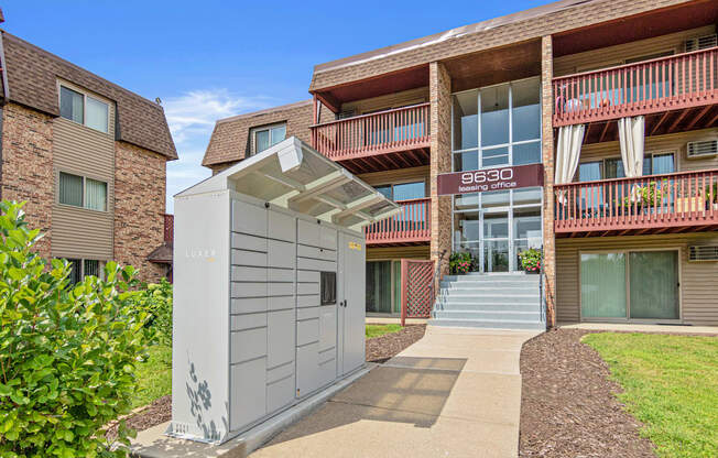 A small white portable building with a grey roof is in front of a brick building.