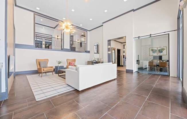 A spacious living room with a white sofa and wooden chairs.