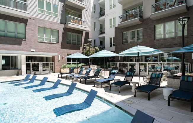 A pool area with chairs and umbrellas in front of apartment buildings.