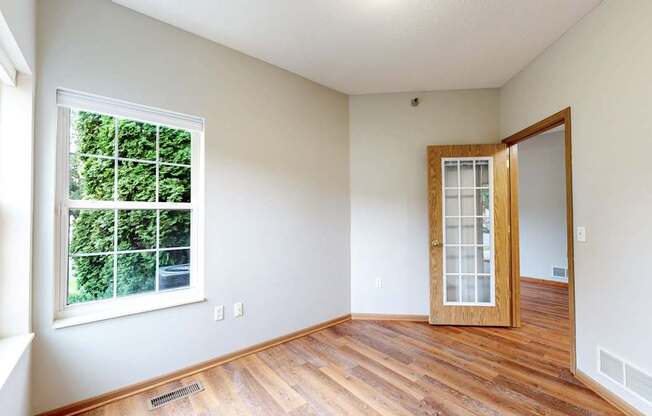 A room with a wooden floor, a window, and a door.
