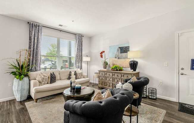 A living room with a grey armchair, a white sofa, a wooden coffee table, and a white vase with a green plant.