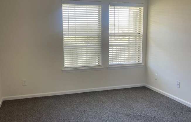 an empty living room with two windows and carpet