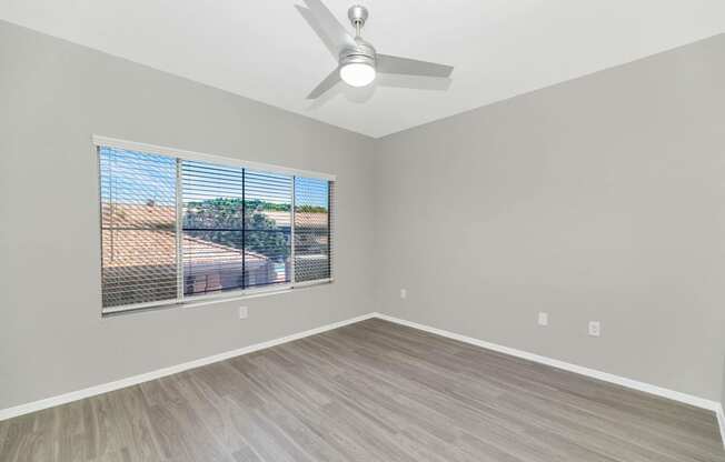 an empty living room with a large window and a ceiling fan
