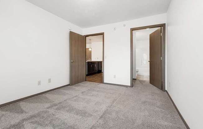 A carpeted room with a white wall and a brown door.