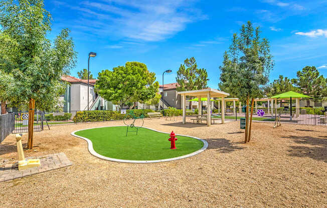 A playground with a red fire hydrant in the middle of a green grassy area.
