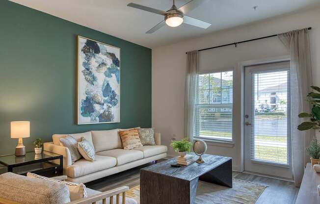 A living room with a couch, a table, a lamp, a plant, and a painting on the wall.