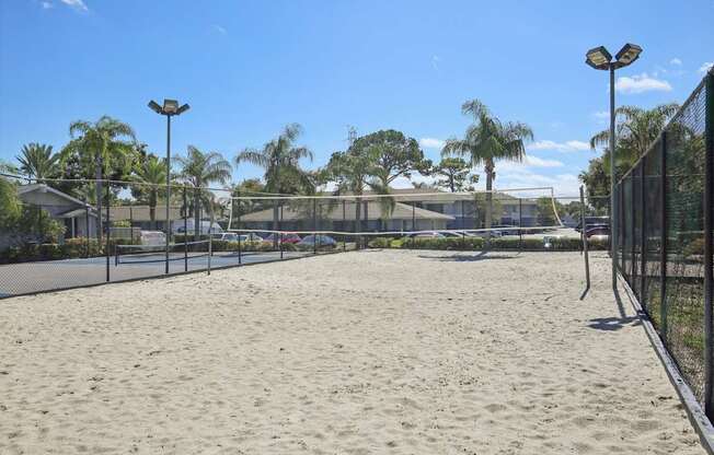 A sandy beach area with a fence and palm trees in the background.