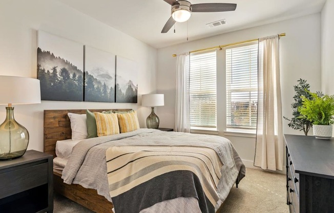 A bedroom with a bed, a ceiling fan, and a painting on the wall.