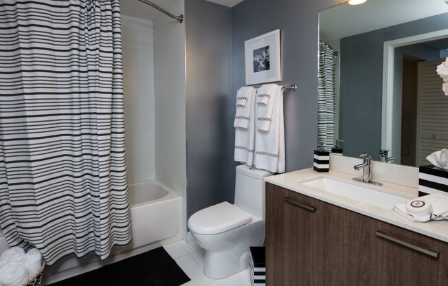 Model bathroom at our apartments in Miami, featuring wood laminate cupboards, white tile floors, and a shower / bath.