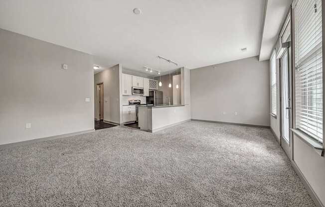 the living room and kitchen of an apartment with a carpeted floor and white walls