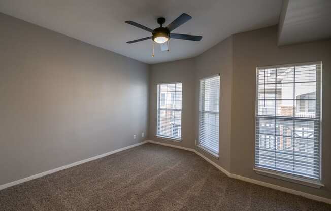 an empty living room with a ceiling fan and three windows
