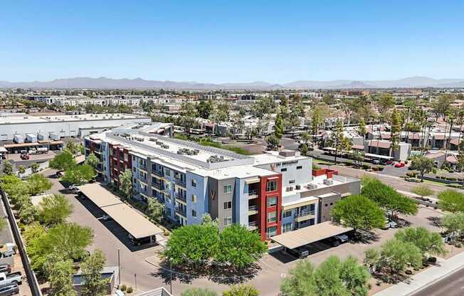 A large building with a red section is surrounded by trees and other buildings.