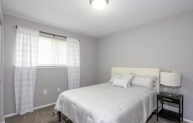 A bedroom with a white bed and a window with curtains.
