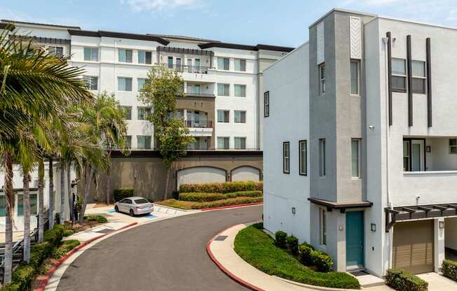 A white building with a blue door is situated on the right side of a curved driveway.