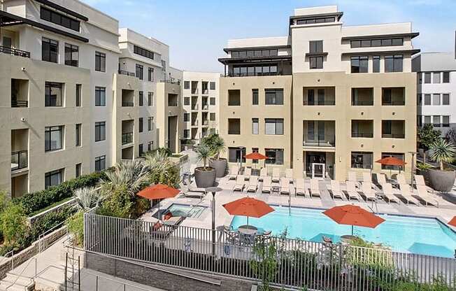 a swimming pool with chaise lounge chairs and umbrellas in front of a building