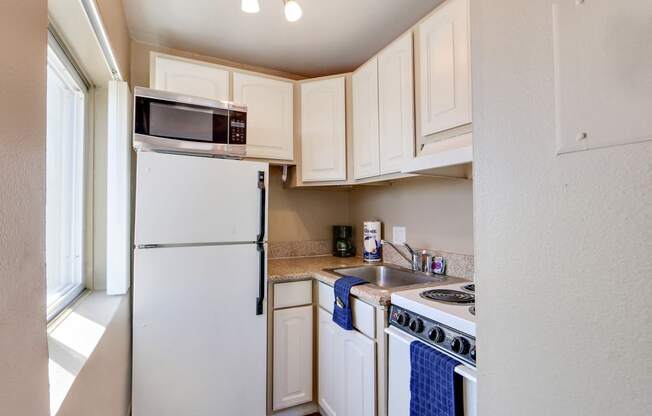 Studio kitchen with two door refrigerator, microwave, electric stove over range hood, and a single kitchen sink with granite countertops