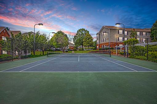 A tennis court is surrounded by a fence and a building.