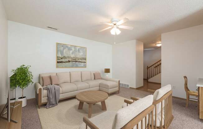 Bismarck Pebble Creek Apartments. The spacious living room is tastefully decorated with stylish furniture, ample natural light, and a cozy atmosphere. There's overhead lighting with a touch of natural light from the dining room. Access to the upstairs is in the background