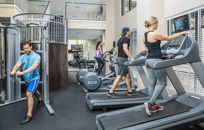 Fitness center with treadmills and lat pull machine. People running on treadmill and using stationary bicycle.