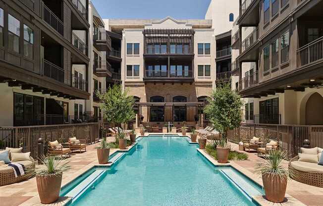A large pool in the middle of a courtyard surrounded by potted plants and lounge chairs.