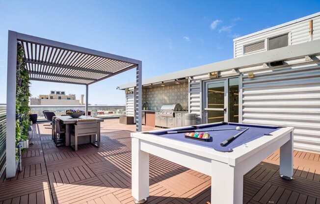 A pool table is on a patio with a table and chairs.