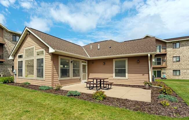 A house with a brown roof and tan siding has a picnic table in front of it.