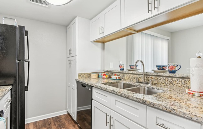 a kitchen with white cabinets and granite counter tops and a black refrigerator