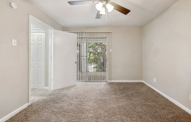 an empty living room with a ceiling fan and a door to a balcony