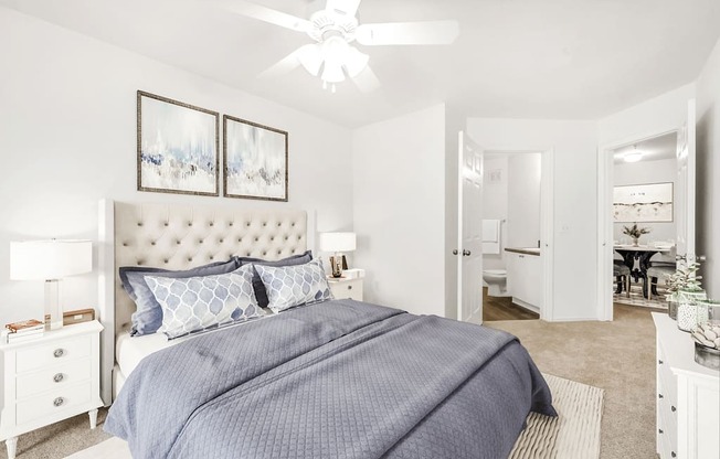 Virtually staged bedroom with carpet, white walls, accent run, ceiling fan with light, white dresser and nightstands with lamps and wall decor