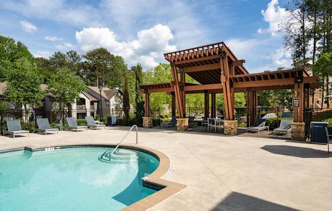 A pool with a wooden pergola and lounge chairs.
