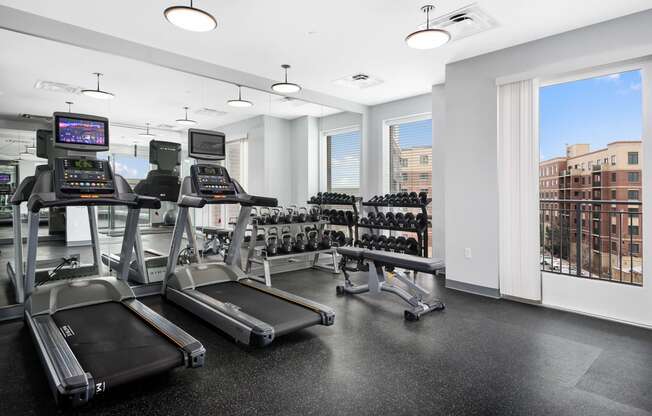 a gym with cardio equipment and a window with a view of the city