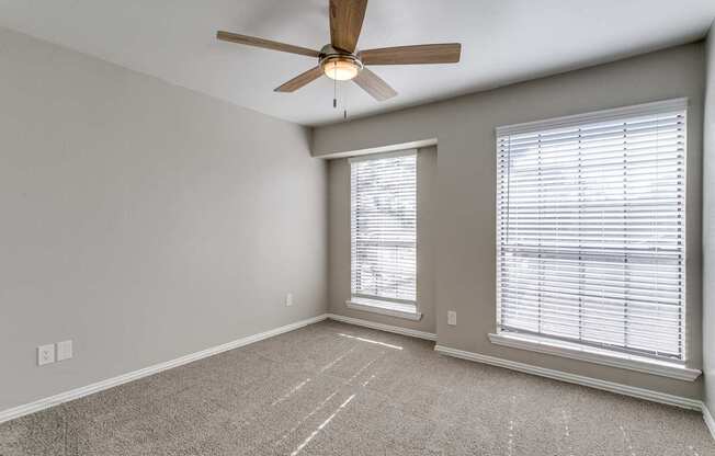 A room with a ceiling fan and two windows with blinds.