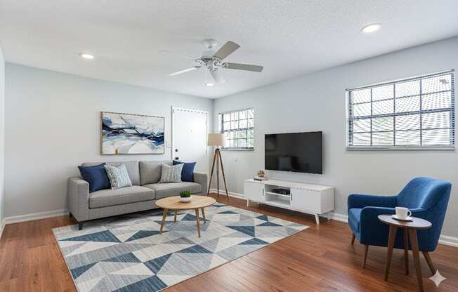 A living room with a grey couch, a blue chair, a wooden coffee table, and a television.