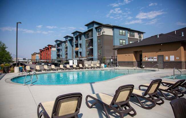 A pool with chairs around it and apartment buildings in the background.