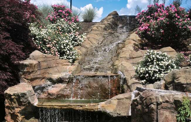 a small waterfall in a rock garden with flowers