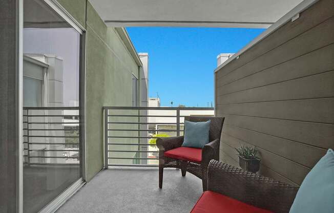 A balcony with a red cushion and a brown chair.